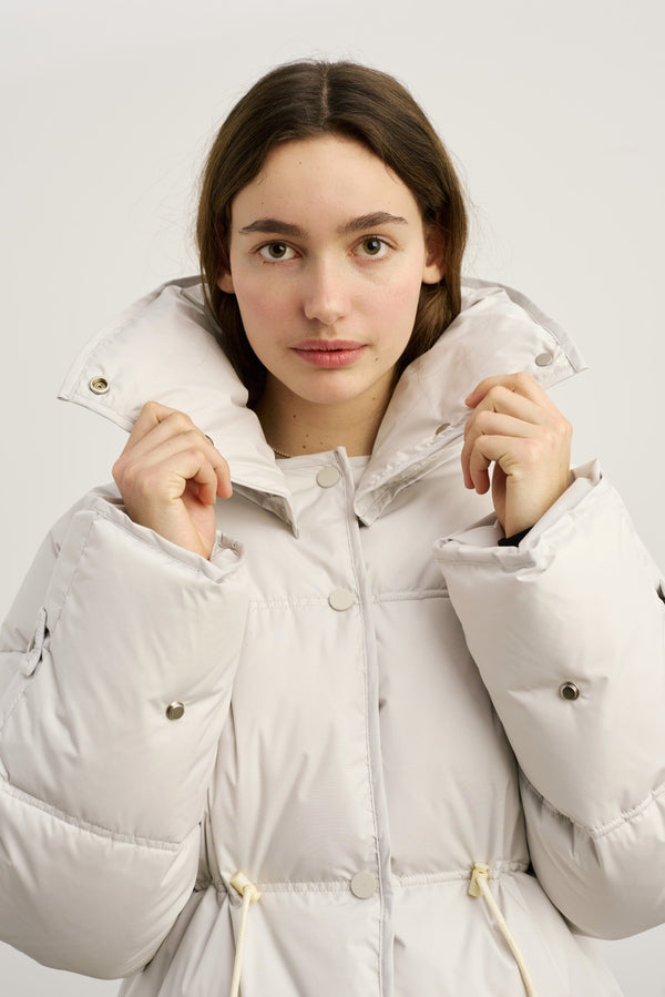 A model wearing a light-colored puffer jacket with a high collar, showcasing the stylish design of MEOTINE outerwear.