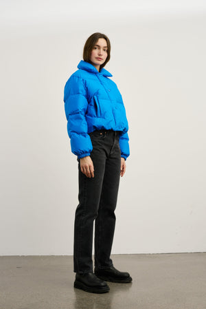 A model wears a vibrant blue cropped puffer jacket paired with black jeans and chunky boots, showcasing MEOTINE's stylish outerwear.