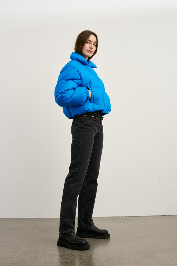 A model wears a vibrant blue puffer jacket paired with black jeans and chunky boots, showcasing MEOTINE's stylish winter collection.