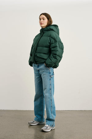 A model stands in a green puffer jacket paired with light blue jeans and sneakers, showcasing MEOTINE's stylish winter wear.