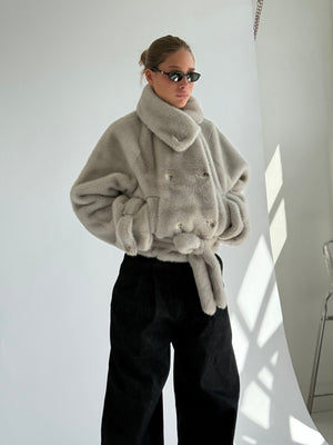 A model showcases a stylish, oversized gray faux fur coat with a belted waist, paired with black wide-leg pants and sunglasses.
