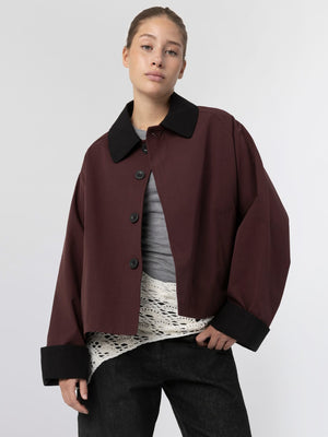 A model wears a burgundy cropped jacket with a black collar, paired with a gray top and textured white layer underneath, showcasing MEOTINE style.