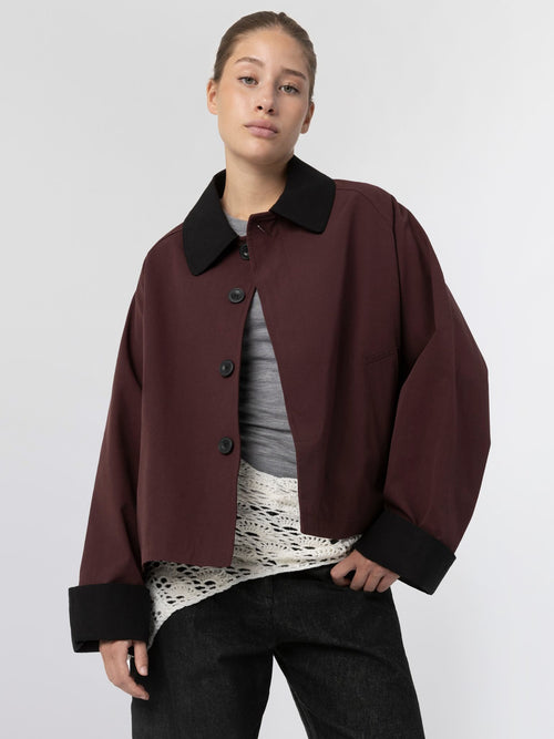 A model wears a burgundy cropped jacket with a black collar, paired with a gray top and textured white layer underneath, showcasing MEOTINE style.