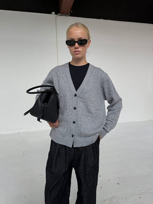 A model wearing a gray cardigan over a black top, holding a black bag, showcasing MEOTINE's stylish and modern aesthetic.