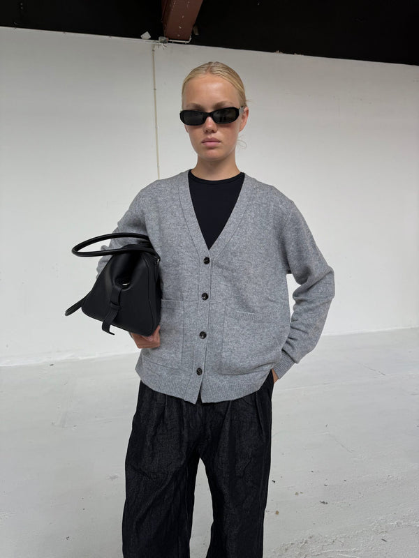A model wearing a gray cardigan over a black top, holding a black bag, showcasing MEOTINE's stylish and modern aesthetic.