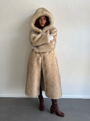 A model wearing a luxurious beige MEOTINE fur coat with a hood, styled with knee-high brown boots against a neutral backdrop.