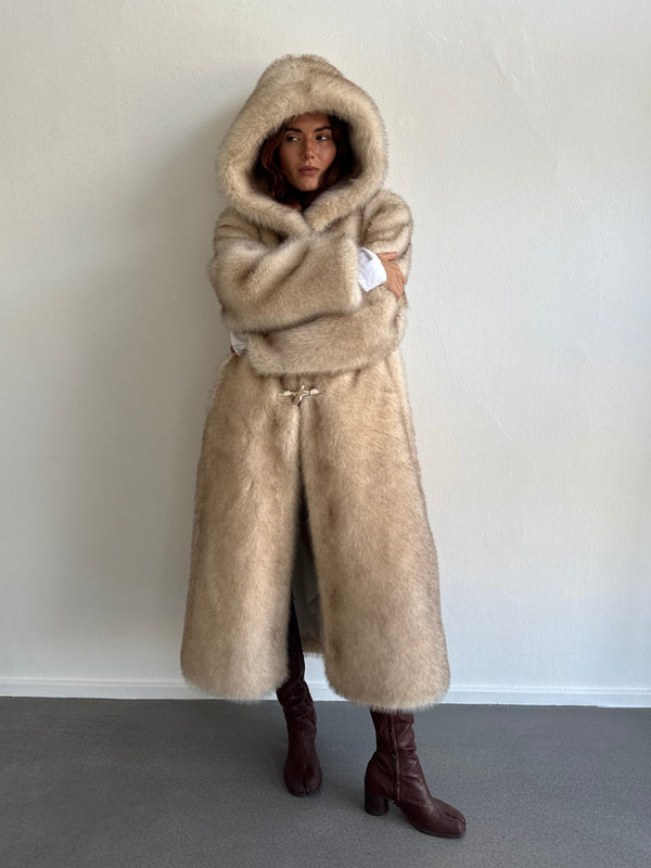A model wearing a luxurious beige MEOTINE fur coat with a hood, styled with knee-high brown boots against a neutral backdrop.