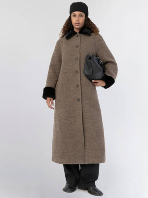 A model wearing a long brown coat with black fur cuffs and collar, holding a black handbag, showcasing MEOTINE's stylish design.