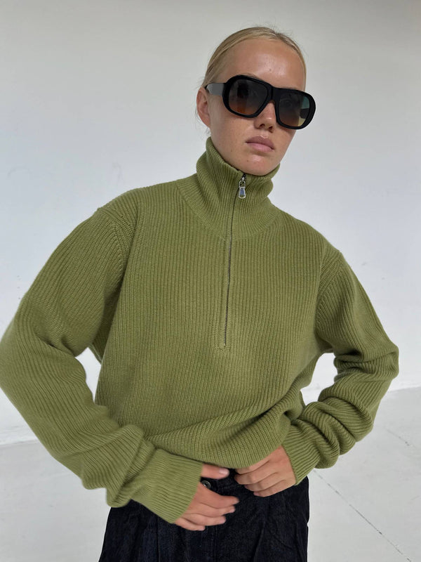 A model wears a stylish olive green ribbed sweater with a high collar and oversized black sunglasses, showcasing MEOTINE's chic design.
