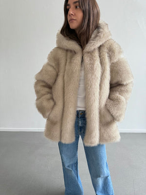 A model wearing a cozy beige faux fur jacket with a hood, paired with light blue jeans, showcasing MEOTINE's stylish design.
