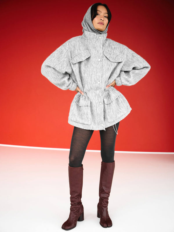 A model showcases a stylish gray oversized jacket with a hood, paired with black leggings and brown knee-high boots, by MEOTINE.