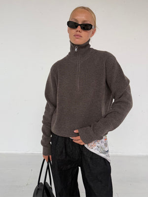 A model wearing a brown zip-up sweater and black sunglasses, paired with loose black pants, showcasing a stylish MEOTINE look.
