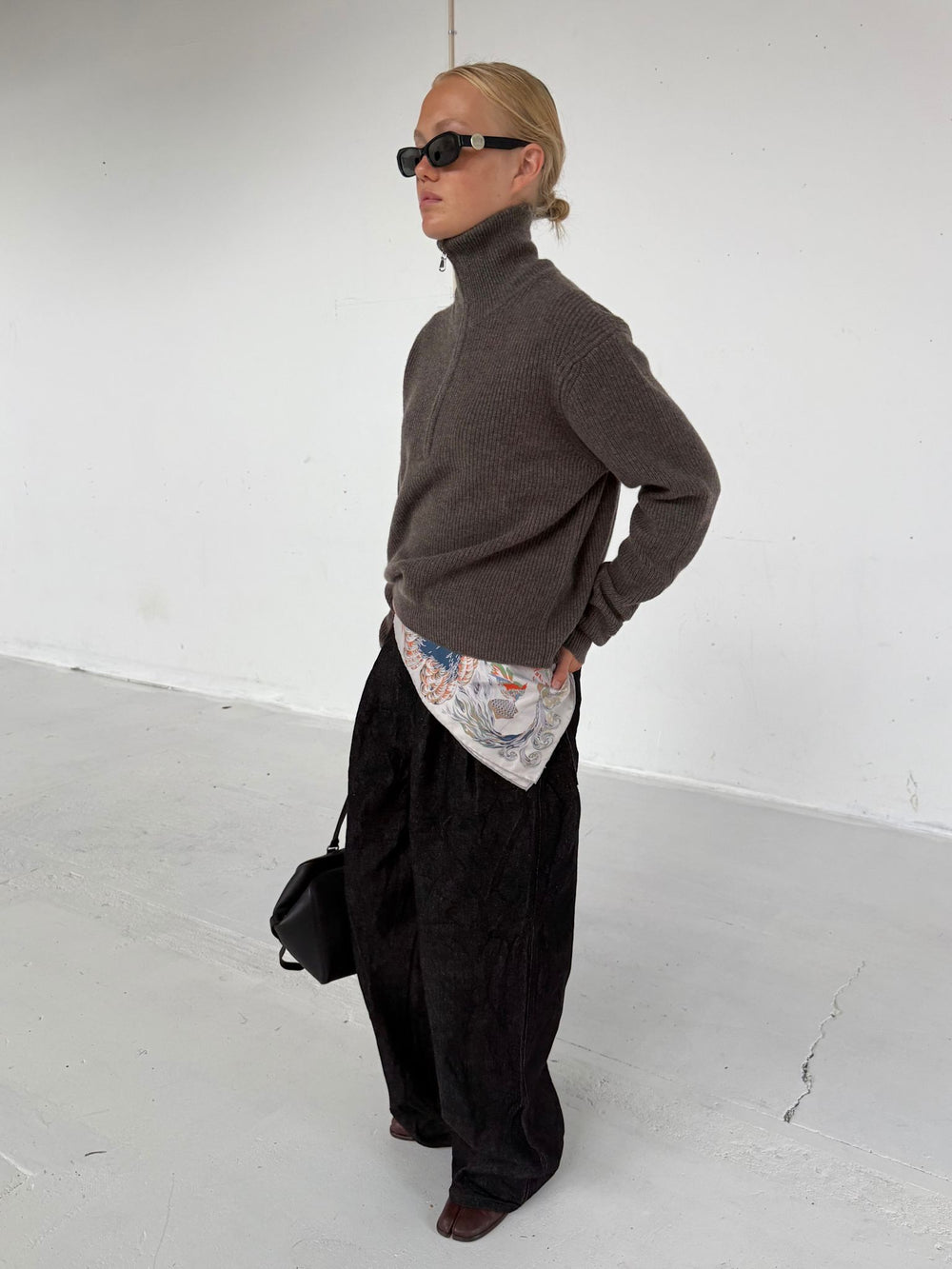 A model wearing a brown zip-up sweater and black sunglasses, paired with loose black pants, showcasing a stylish MEOTINE look.