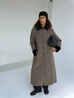 A model wearing a stylish brown coat with black accents, holding a black handbag, showcasing MEOTINE's elegant design.
