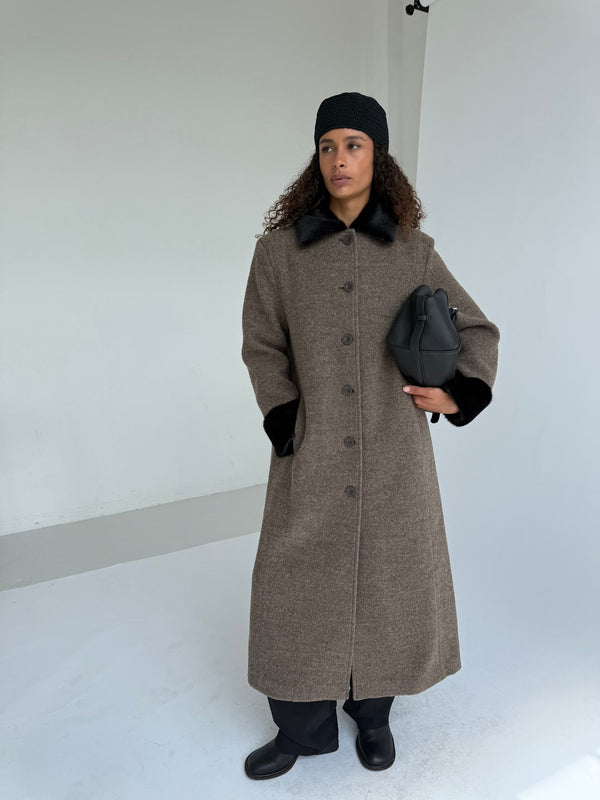 A model wearing a stylish brown coat with black accents, holding a black handbag, showcasing MEOTINE's elegant design.