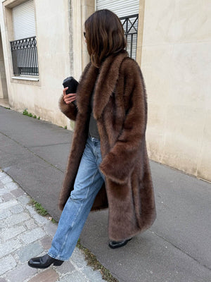 A woman walks down the street in a luxurious brown fur coat, paired with jeans and black boots, showcasing MEOTINE's elegant style.