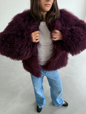 A model wears a fluffy, burgundy MEOTINE jacket over a white top, paired with light blue jeans and black shoes.