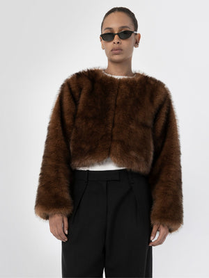 A model wears a stylish brown faux fur cropped jacket by MEOTINE, paired with black high-waisted trousers and sunglasses.