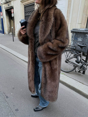 A woman wearing a luxurious brown fur coat, styled with casual jeans and black boots, exuding elegance and warmth. MEOTINE.