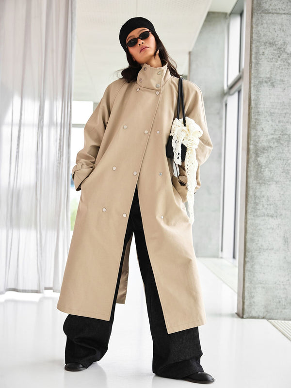 A model showcases a stylish beige trench coat by MEOTINE, paired with wide-leg black pants and accessories, exuding modern elegance.