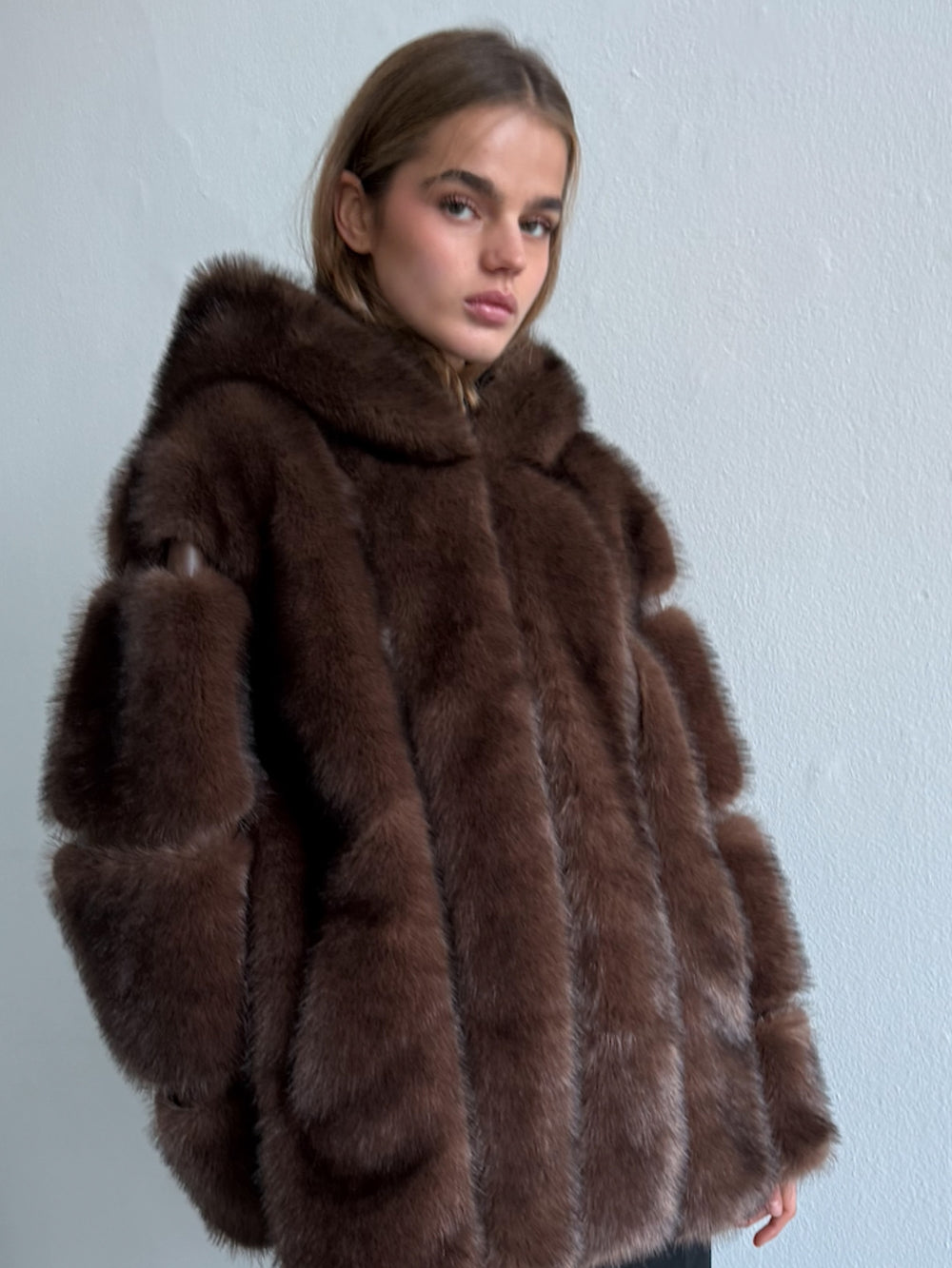 Woman wearing a brown fur coat against a light gray background