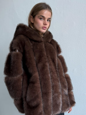 Woman wearing a brown fur coat against a light gray background