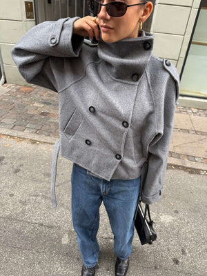 A stylish individual wearing a gray MEOTINE jacket with a high collar, paired with blue jeans and sunglasses, on a city street.