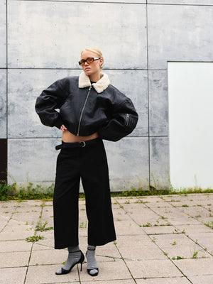 A model showcases a stylish black leather bomber jacket with a fur collar, paired with wide-leg black trousers and chic heels.