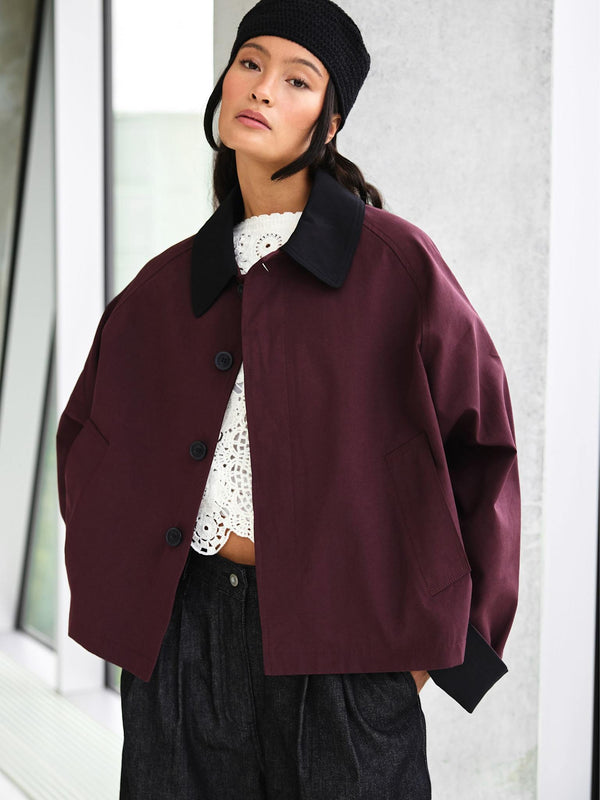 A model showcases a stylish burgundy oversized jacket with a black collar, paired with a white lace top and dark trousers, by MEOTINE.