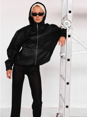 A model poses in a black leather hoodie with a zip, paired with sleek black pants, showcasing a stylish urban look for MEOTINE.