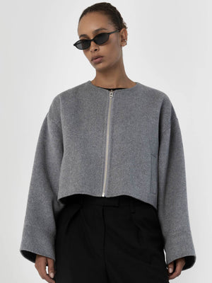 A model wears a cropped gray jacket with a zip front and wide sleeves, paired with black trousers and stylish sunglasses. MEOTINE.