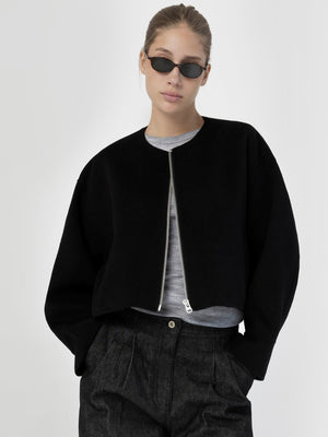 A model wearing a black cropped jacket with a zip front, paired with a gray top and stylish sunglasses, showcasing MEOTINE's modern design.