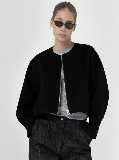 A model wearing a black cropped jacket with a zip front, paired with a gray top and stylish sunglasses, showcasing MEOTINE's modern design.