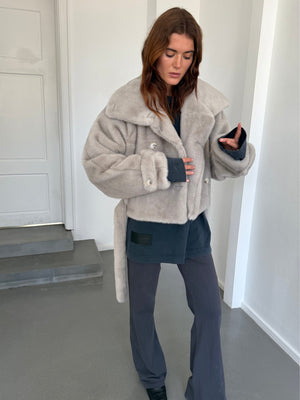 A model showcases a cozy, oversized gray faux fur jacket from MEOTINE, paired with a dark top and relaxed pants.