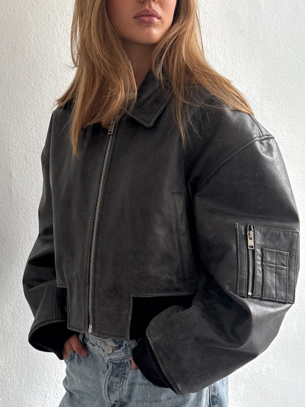 Stylish black leather cropped jacket with a relaxed fit, featuring a zip closure and ribbed cuffs, perfect for a trendy look. MEOTINE.