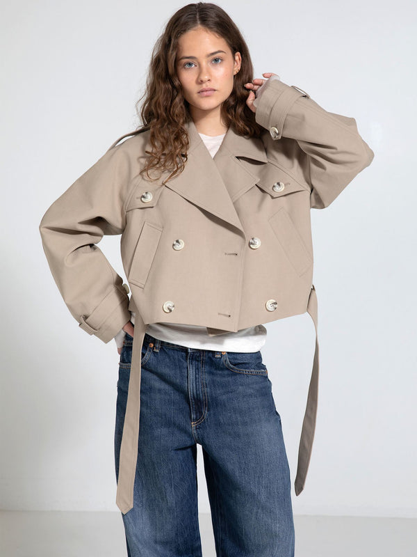A model showcases a stylish beige cropped jacket with a double-breasted design and tie details, paired with loose jeans. MEOTINE.