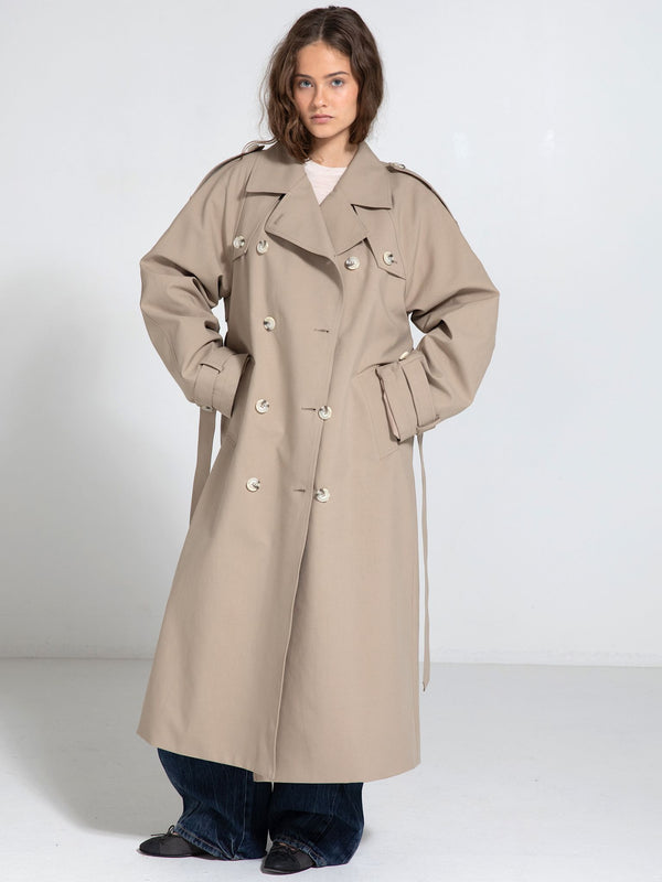 A model showcases a stylish beige trench coat with a double-breasted design, featuring a relaxed fit and wide sleeves by MEOTINE.
