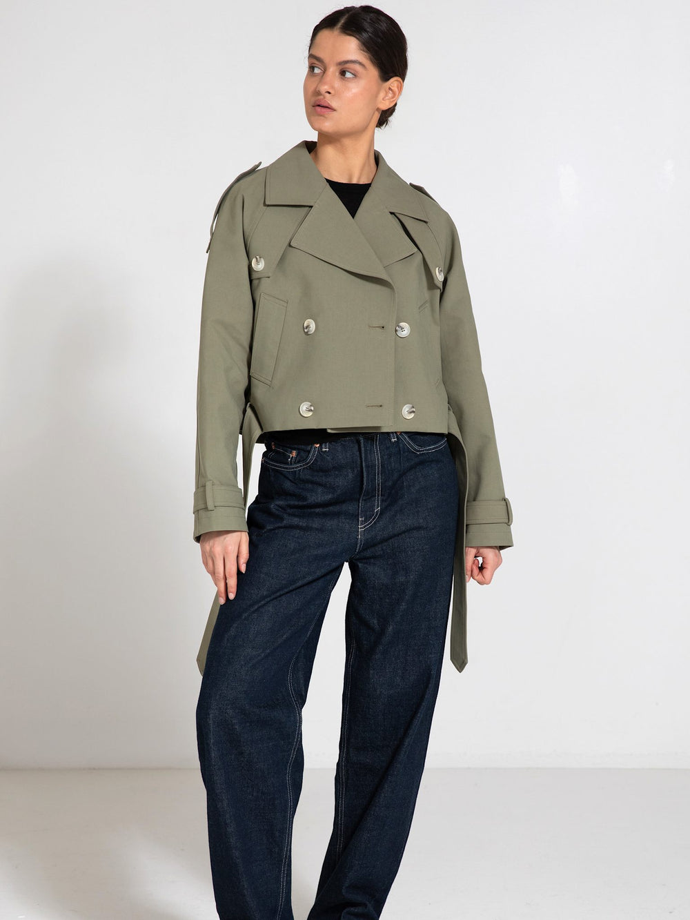 A model wears a stylish cropped olive green trench coat with oversized buttons, paired with loose-fitting dark jeans. MEOTINE.