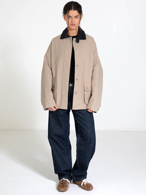 A model stands in a spacious room wearing a beige MEOTINE jacket with a black collar, paired with loose blue jeans and brown shoes.