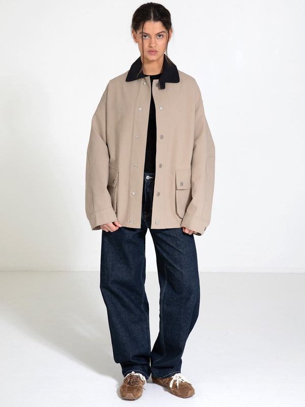 A model stands in a spacious room wearing a beige MEOTINE jacket with a black collar, paired with loose blue jeans and brown shoes.