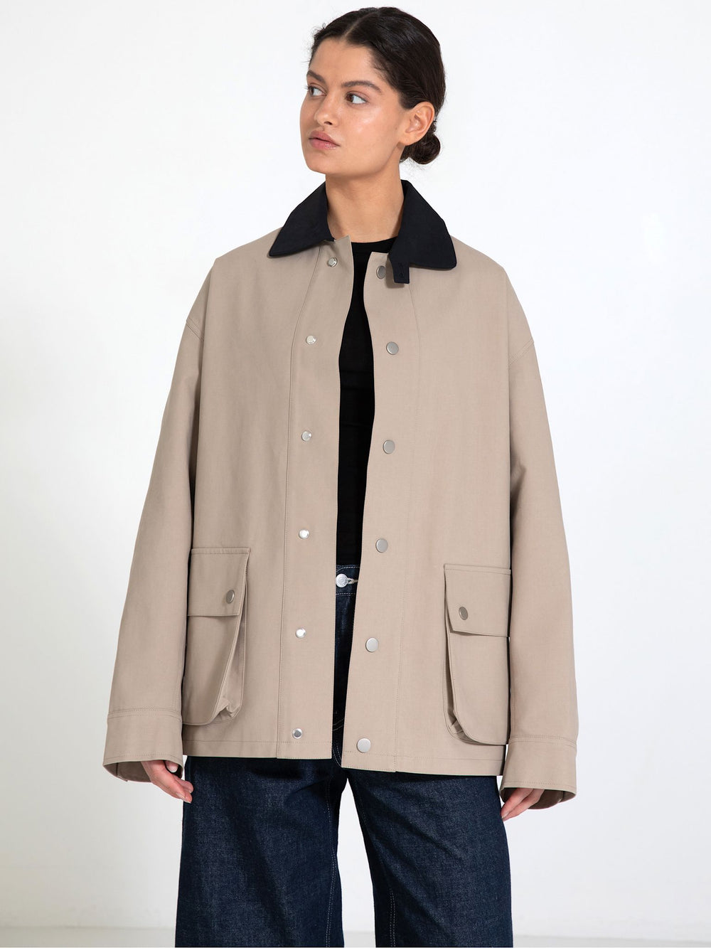 A model stands in a spacious room wearing a beige MEOTINE jacket with a black collar, paired with loose blue jeans and brown shoes.