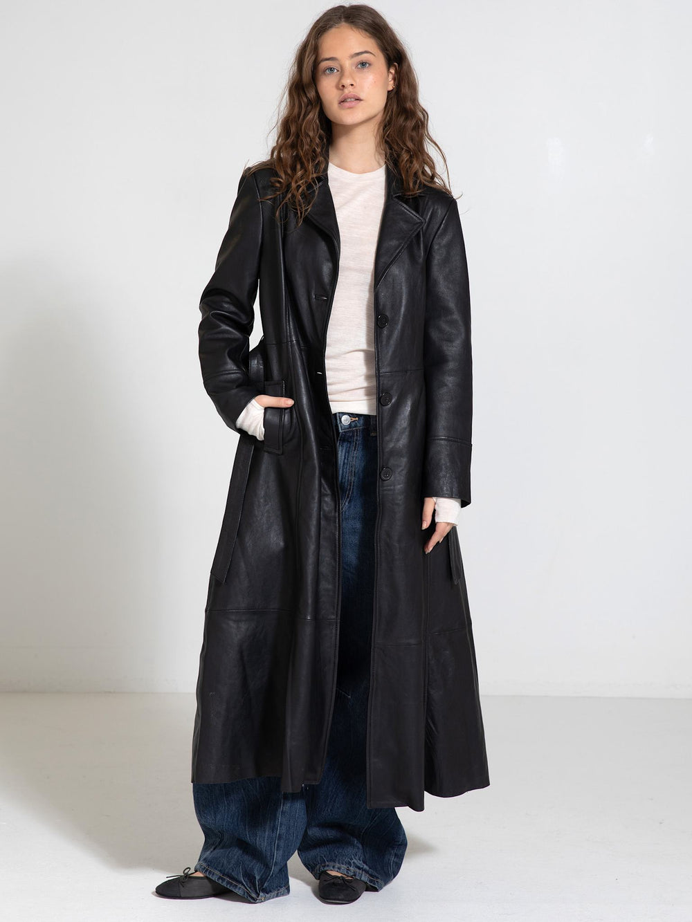 A model showcases a stylish black leather coat from MEOTINE, paired with a light top and wide-leg jeans, set against a plain background.