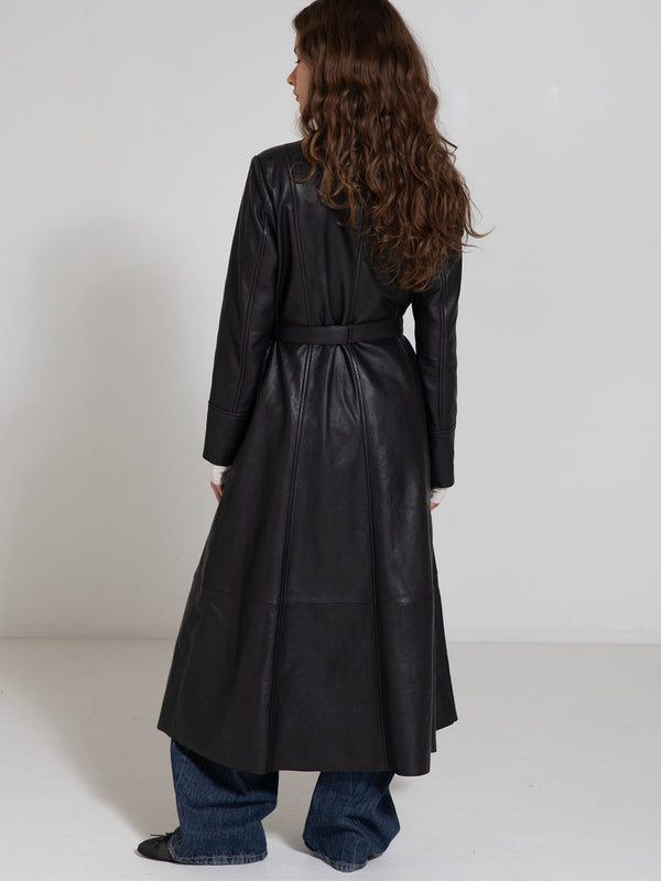 A woman in a long black leather coat with a belted waist, styled with wide-leg jeans, showcasing MEOTINE's chic design.