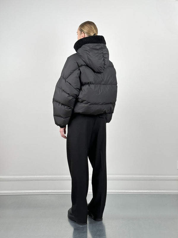A model wearing a black puffer jacket with a high collar and hood, paired with loose black pants, showcasing MEOTINE's stylish design.