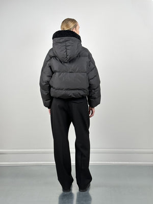 A model wearing a black puffer jacket with a hood, paired with black pants, showcasing a stylish winter look by MEOTINE.