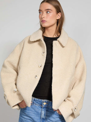 A model wears a cozy beige MEOTINE jacket with a button-up front, paired with a black top and blue jeans, exuding casual style.