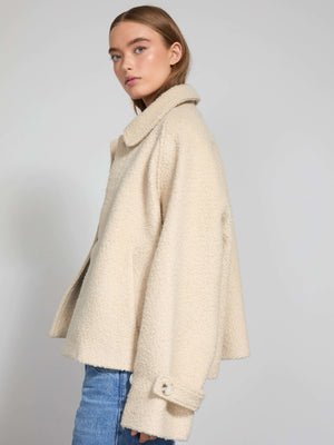 A model showcases a stylish cream-colored MEOTINE jacket with a relaxed fit and oversized collar, paired with blue jeans.