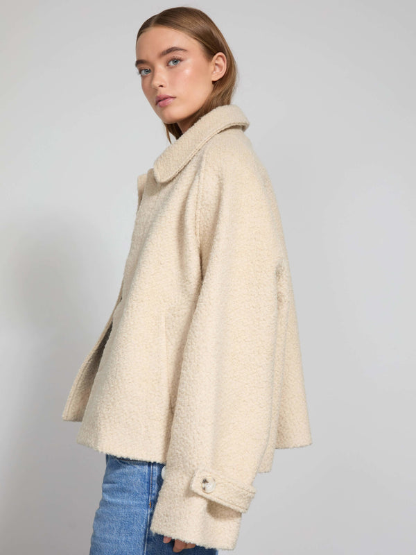 A model showcases a stylish cream-colored MEOTINE jacket with a relaxed fit and oversized collar, paired with blue jeans.