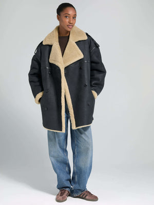 A model showcases a stylish black and beige MEOTINE coat, featuring a plush collar and relaxed fit, paired with casual jeans.