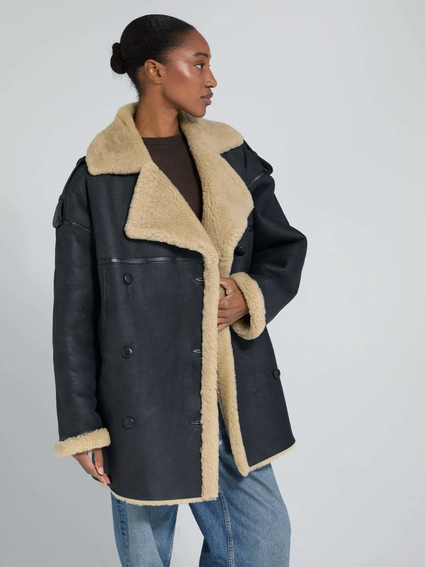 A model showcases a stylish black coat with a beige shearling collar and lining, featuring a double-breasted design by MEOTINE.